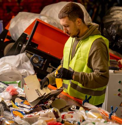 Side view of a sorter in gloves and a protective vest who sorts garbage on a special sorting line while working at a waste disposal station